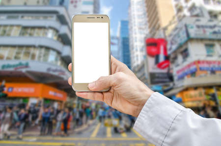Mockup image of hand holding gold mobile phone with blank white screen and blurred city in the backgroundの写真素材