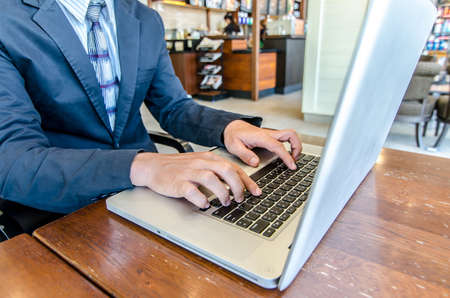 Close-up of business man hands on laptop keyboard. On wooden table is a smartphone .Man is shopping online. Young man surf the Internet on your computer.の写真素材