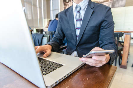 Business man mobile phone and laptop computer in coffee shop. City lifestyle business man hands working on typing on smartphone using 4G 5G wifi internet online service.の写真素材