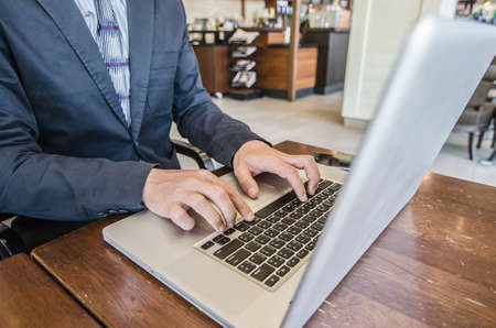 Close-up of business man hands on laptop keyboard. On wooden table is a smartphone .Man is shopping online. Young man surf the Internet on your computer.の写真素材