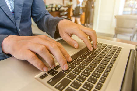Close-up of business man hands on laptop keyboard. On wooden table is a smartphone .Man is shopping online. Young man surf the Internet on your computer.の写真素材