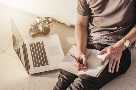 man write pen on notebook and work on laptop, a man relax working from home using  notebook computer and camera, businessman planning business at his workplace and search data by laptop and internetの写真素材