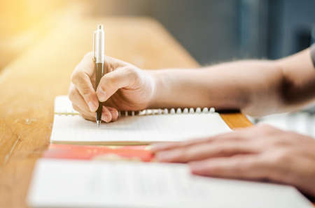 Close up of student hand writing on book with pen