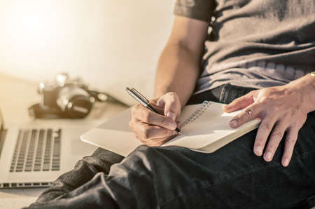 man write pen on notebook and work on laptop, a man relax working from home using  notebook computer and camera, businessman planning business at his workplace and search data by laptop and internetの写真素材