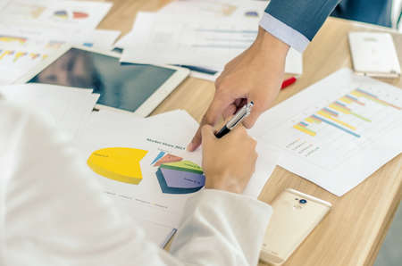 Close-up of business team image of male hand pointing at business document during discussion at meeting and using pen with financial diagram and digital tabletの写真素材