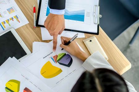 Close-up of business team image of male hand pointing at business document during discussion at meeting and using pen with financial diagram and digital tabletの写真素材
