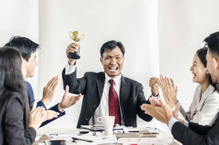 winning business team with a man executive holding a gold trophy . happy and successful business team rewarded for in the officeの写真素材