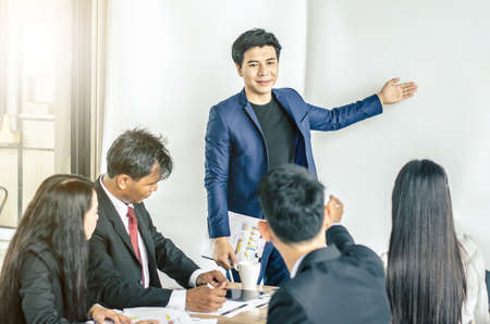 Photo of successful young manager standing making a presentation financial diagram while the others listening to himの写真素材
