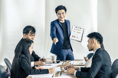 Photo of successful young manager standing making a presentation financial diagram while the others listening to himの写真素材