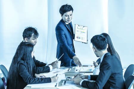 Photo of successful young manager standing making a presentation financial diagram while the others listening to himの写真素材