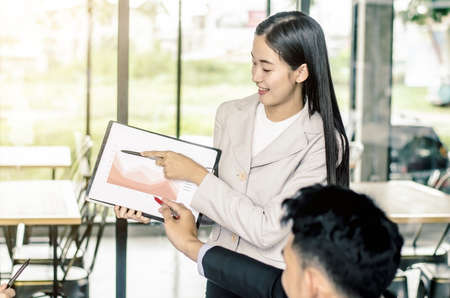 Photo of successful young manager standing making a presentation financial diagram while the others listening to herの写真素材