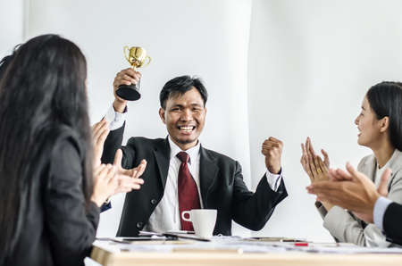 winning business team with a man executive holding a gold trophy . happy and successful business team rewarded for in the officeの写真素材