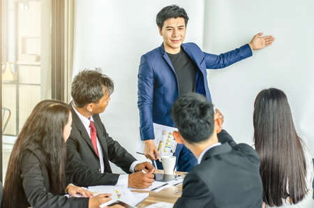 Photo of successful young manager standing making a presentation financial diagram while the others listening to himの写真素材
