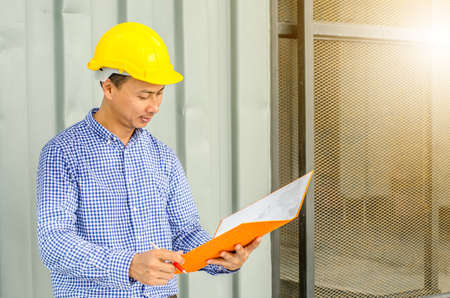 Asian Electrical Engineer holding files while wearing a personal protective equipment safety helmet...