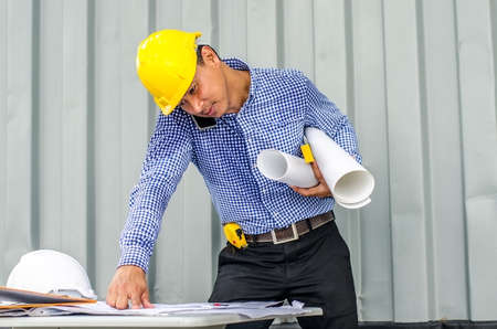 Busy construction engineer talking on phone while carrying blueprints with checking the building progressの写真素材