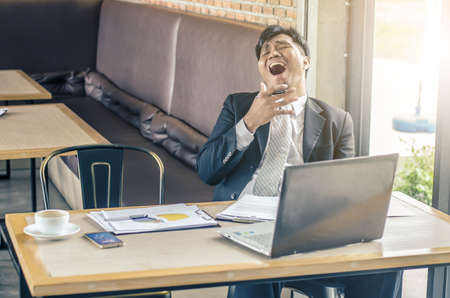 Tired man yawning at workplace in coffee shopの写真素材
