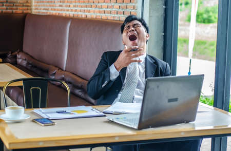 Tired man yawning at workplace in coffee shopの写真素材