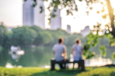 blurred and soft focus, a girl and a man sitting on a Park bench by the lake. The blurred and bokeh backgroundの写真素材