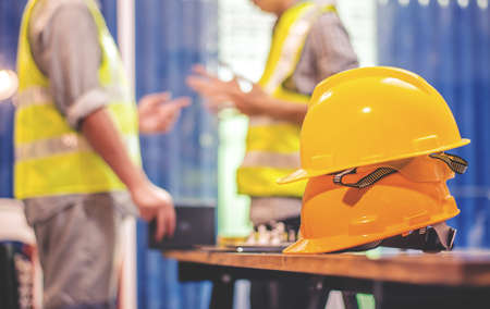 Yellow hard safety helmet hats for safety project of workman as engineer or worker, Two construction engineers talking at construction site with blueprint on table.の写真素材