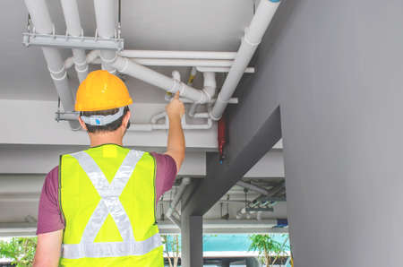 Busy engineer inspectors discussing pipes of new building while examining it at construction site. Rear view of professional engineers in work helmets. Housing project conceptの写真素材