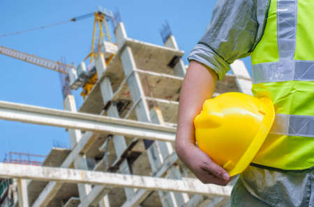 Close-up construction worker holding hard hat with background of blurred construction site.の写真素材