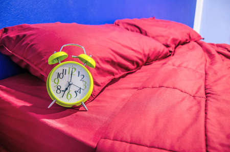 Green alarm clock on red bed in bedroomの写真素材