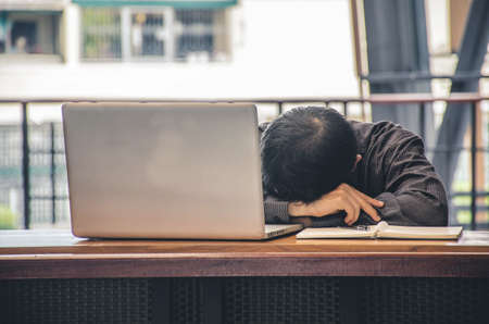 Tired businessman sleeping at his working place office with head on the desk near monitor of computer.の写真素材