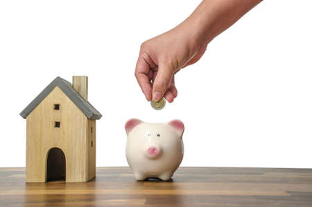 Investor hand hold a coin with save in the piggy bank put on the money on home model for family background,Saving moneyの写真素材