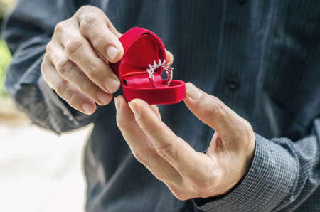 Wedding ring in a special box, holds in the hands of the groom. Man gives a ring with a diamond in a red box.の写真素材
