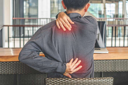 close up of man touches neck feeling pain in the neck and suffering from backache, rear view, man felling exhausted while sitting at his working in the officeの写真素材