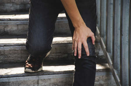 Hand of the boy holding the knee because of injury pain in leg, can not walk up the stairs.の写真素材
