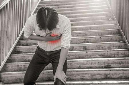 close-up young man walk up the stairs feeling a big pain on the chest with hand touching her chest,...