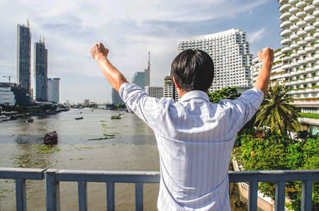 A  businessman is proud for the successful of company and his job. Hand up in the air and feeling powerful,happy, success and achievement concepts , City background.の写真素材