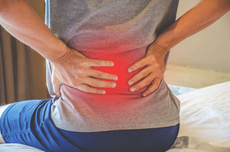 Man suffering from back pain at home in the bedroom. Uncomfortable mattress and pillow causes back pain.の写真素材
