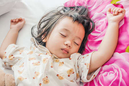 Sleeping baby or infant girl on bed in bedroom with teddy bear in her arms.の写真素材