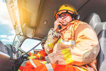 A firefighter in protective clothing and a helmet sits in a cargo rescue vehicle and talks on the...