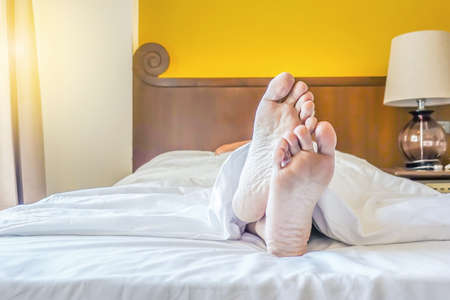 Young male sleeping in bed at hotel with focus on legs. Feet of man lying on bed.