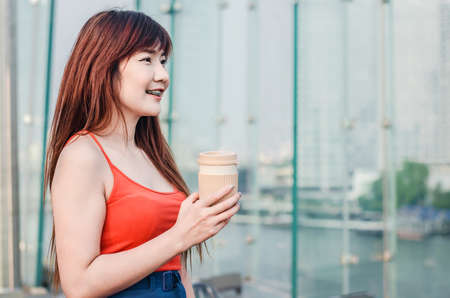 Beautiful young woman standing on balcony having cup of coffee, enjoying sun on a hot summer day....