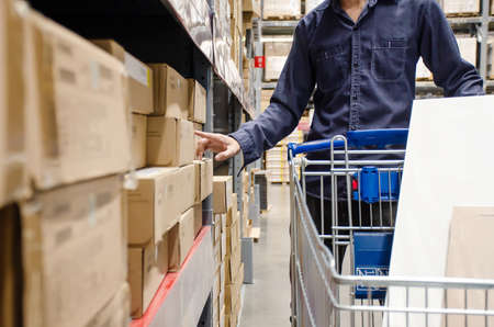 Buyer man with shopping cart in store between row of shelves with goods in department store shopping...