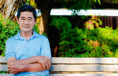 Happy asian senior gentleman sitting on a wooden bench and relaxing in a park  on a sunny day
