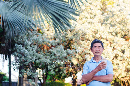 Asian senior gentleman standing in park and drinking coffee with relaxing on a sunny dayの写真素材