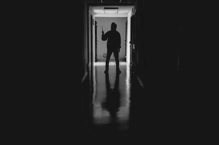 murder, kill and people concept - Criminal or murderer wearing a mask in silhouette holding knife inside a condo at crime sceneの写真素材