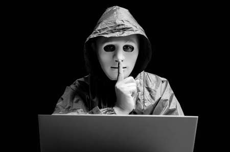 Anonymous computer hacker in white mask and hoodie. Obscured dark face making silence gesture on...