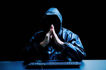 Anonymous computer hacker in white mask and hoodie. Obscured dark face with keyboard computer in the...