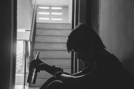 The silhouette of young men holding a bottle of alcohol beer at the old condo, Unhealthy Lifestyle, Addicted Men, Sitting Alone, Depressed Guy with Bottle, Addicted by Alcohol.の写真素材