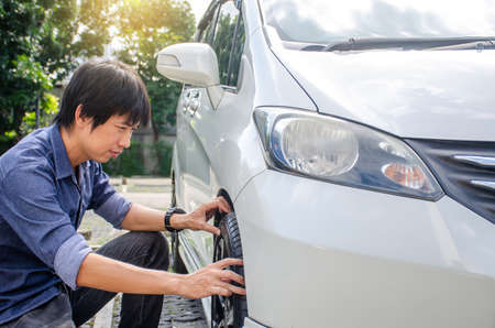 Young man has problems with the wheel of his car. He is kneeing and Check tires before leaving.man checking car conditionの写真素材
