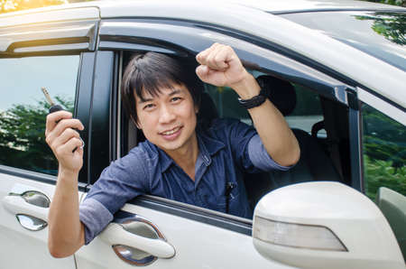 Closeup portrait happy, smiling, young asian man, buyer sitting in his new a car showing car key ,the concept of buying a used car or a rental car, Personal transportationの写真素材