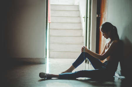 Silhouette of girl sitting alone in the dark,Sad and Serious women sitting hug his knee alone of old condo, Domestic violence, family problems, Stress, violence, The concept of depression and suicidewith copy spaceの写真素材