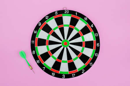 Green dart arrow and dartboard, on pink pastel background. Flat lay. Copy space