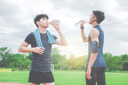 Two young man drinking water from bottle after run. Two young man with bottles of cold drink outdoorsの写真素材